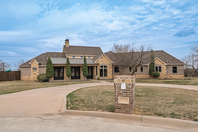 view of front facade featuring curved driveway, a chimney, a front yard, a standing seam roof, and metal roof