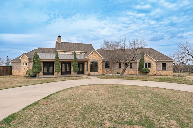 view of front of home with metal roof, concrete driveway, a front lawn, a standing seam roof, and a chimney