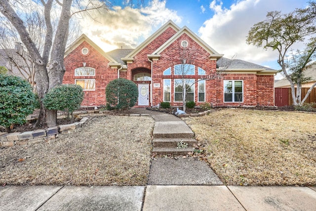 view of front of property with roof with shingles, a front yard, fence, and brick siding