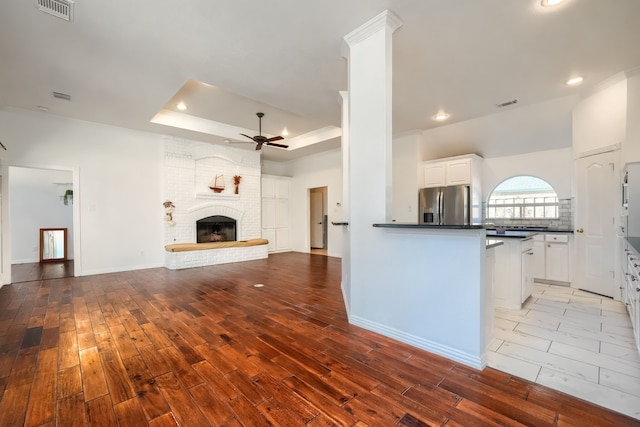 kitchen with a tray ceiling, dark countertops, visible vents, ceiling fan, and stainless steel fridge