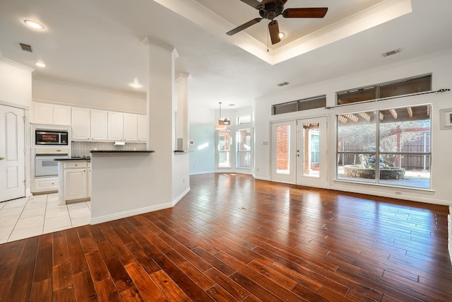 unfurnished living room with wood finished floors, visible vents, ornamental molding, a tray ceiling, and plenty of natural light