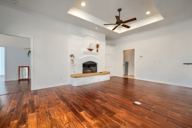 unfurnished living room with crown molding, a raised ceiling, a fireplace, and wood-type flooring