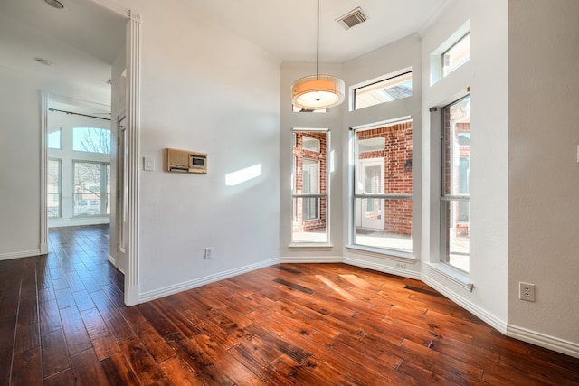 interior space with a high ceiling, dark wood-style flooring, visible vents, baseboards, and crown molding