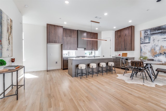 kitchen with beverage cooler, an island with sink, light wood-style flooring, a kitchen breakfast bar, and a sink