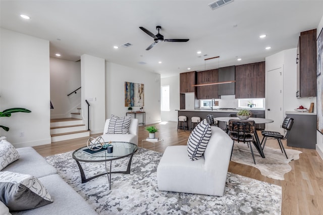 living area with light wood-type flooring, recessed lighting, visible vents, and stairs