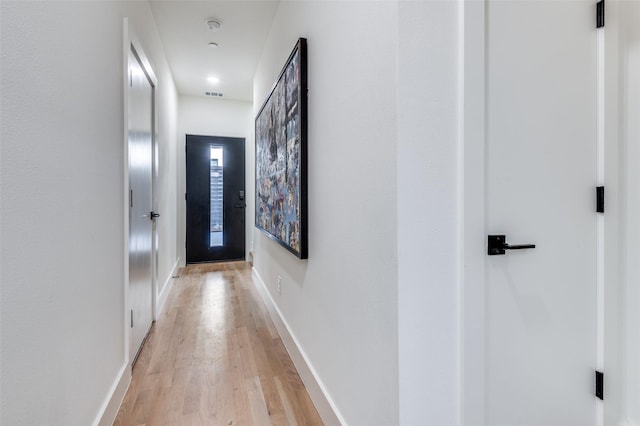 corridor with light wood-style flooring, visible vents, and baseboards