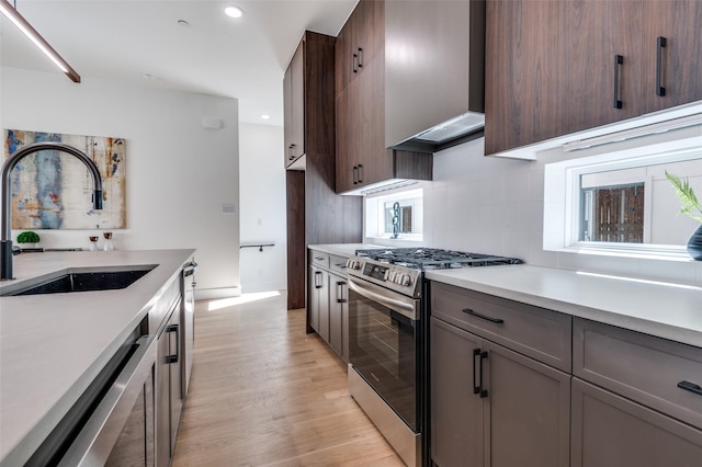 kitchen with dishwasher, custom exhaust hood, light countertops, stainless steel range with gas cooktop, and a sink