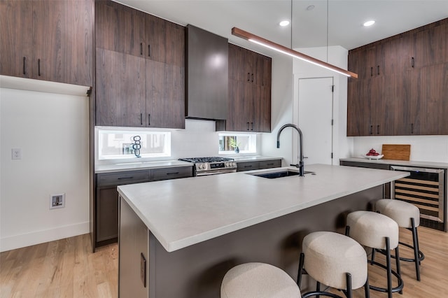 kitchen featuring stainless steel gas stove, light wood finished floors, wine cooler, a kitchen breakfast bar, and a sink