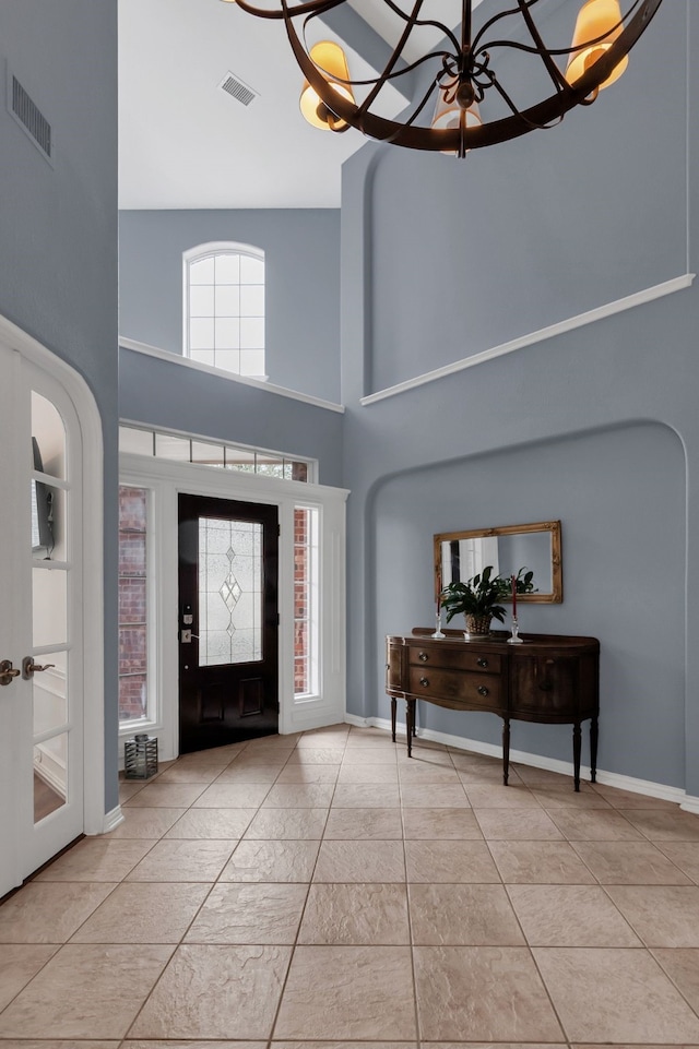 foyer with visible vents, an inviting chandelier, a towering ceiling, and light tile patterned floors