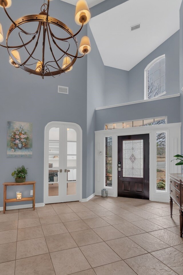 tiled foyer featuring visible vents, arched walkways, an inviting chandelier, and a towering ceiling