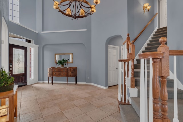 entryway featuring light tile patterned floors, arched walkways, a towering ceiling, stairway, and a notable chandelier