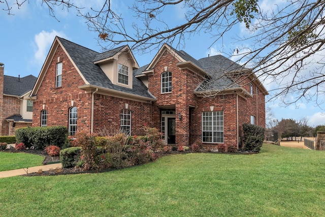 traditional-style house with roof with shingles, a front yard, and brick siding