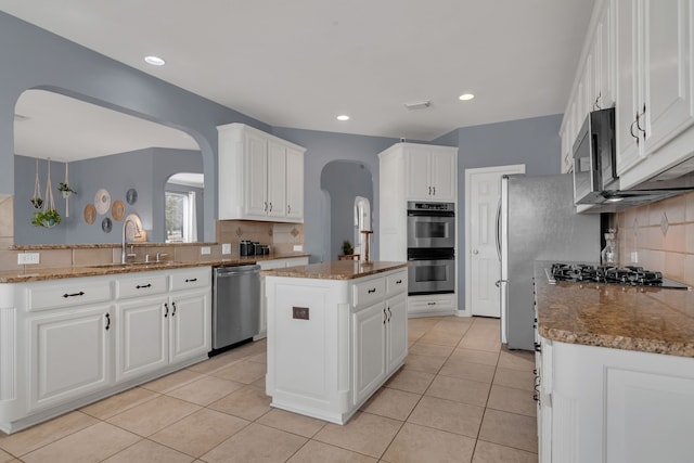 kitchen featuring light tile patterned floors, arched walkways, a sink, appliances with stainless steel finishes, and backsplash