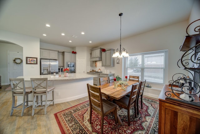 dining area with baseboards, an inviting chandelier, recessed lighting, arched walkways, and light wood-style floors