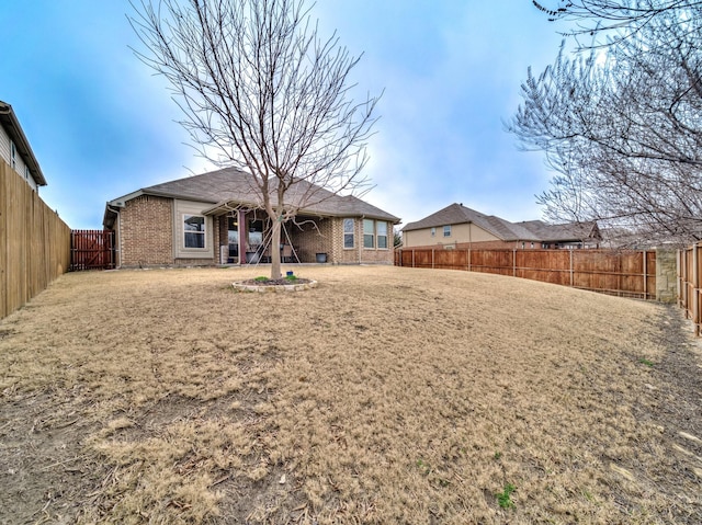 rear view of property featuring brick siding, a fenced backyard, and a lawn