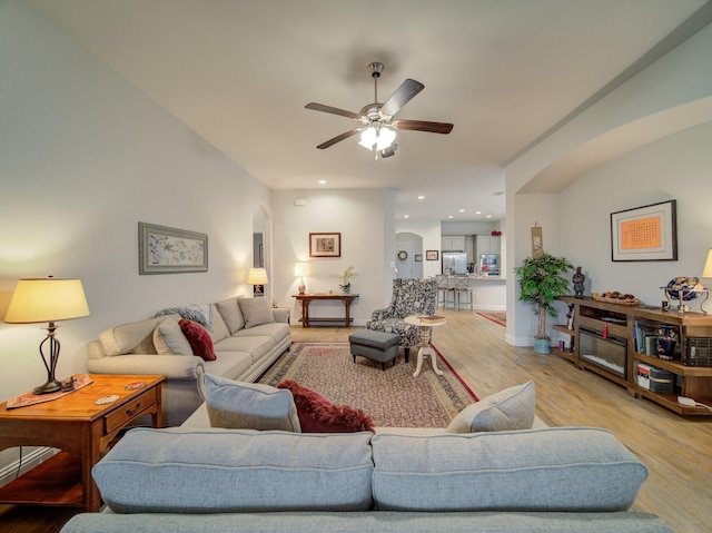 living area featuring baseboards, wood finished floors, arched walkways, and ceiling fan