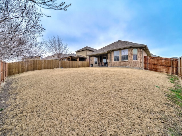 rear view of house with brick siding, a patio area, and a fenced backyard