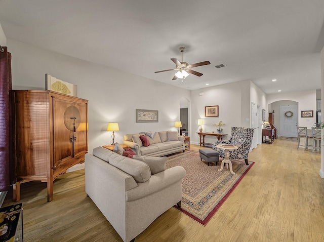 living room featuring light wood-style flooring, visible vents, arched walkways, and ceiling fan