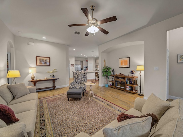 living room featuring baseboards, light wood-type flooring, recessed lighting, arched walkways, and a ceiling fan