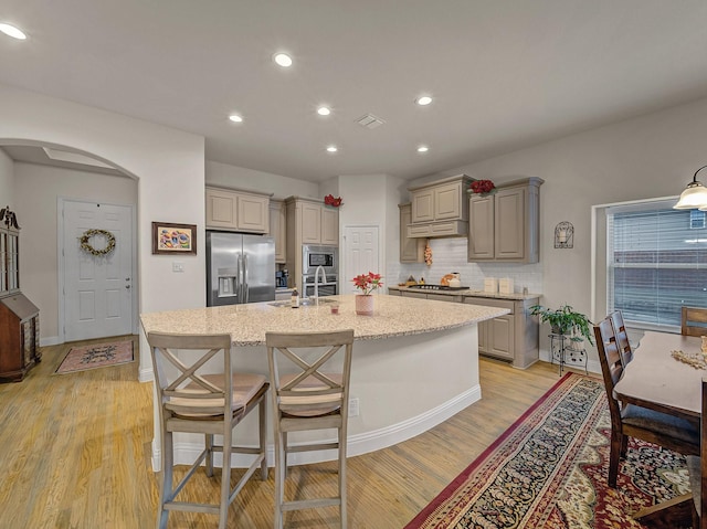 kitchen with a center island with sink, light wood-style flooring, arched walkways, gray cabinetry, and appliances with stainless steel finishes