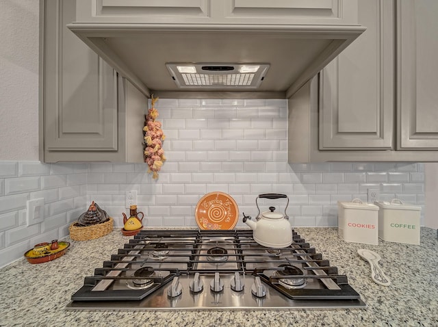 kitchen with tasteful backsplash, gray cabinetry, ventilation hood, stainless steel gas cooktop, and light stone counters