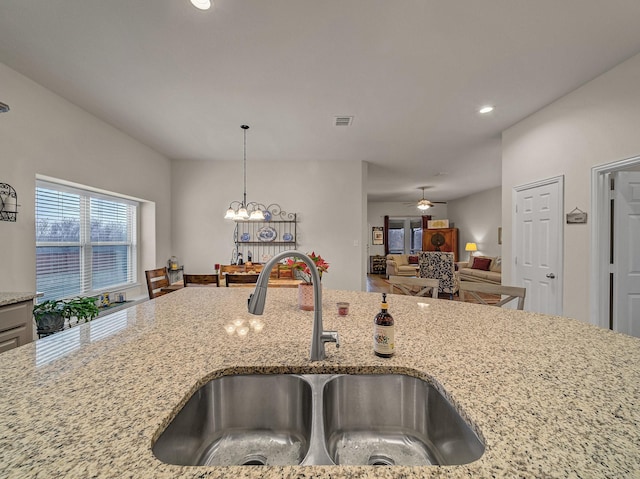 kitchen featuring ceiling fan with notable chandelier, light stone countertops, visible vents, and a sink