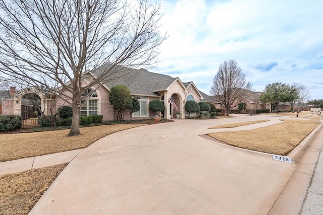 view of front of home with driveway, brick siding, stone siding, and fence