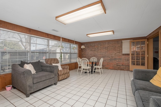 living room with brick wall, wood walls, light tile patterned flooring, and visible vents