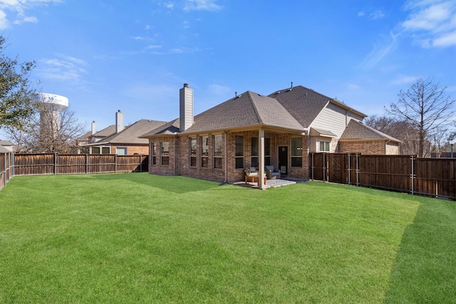 rear view of property featuring a lawn, a fenced backyard, a chimney, roof with shingles, and brick siding