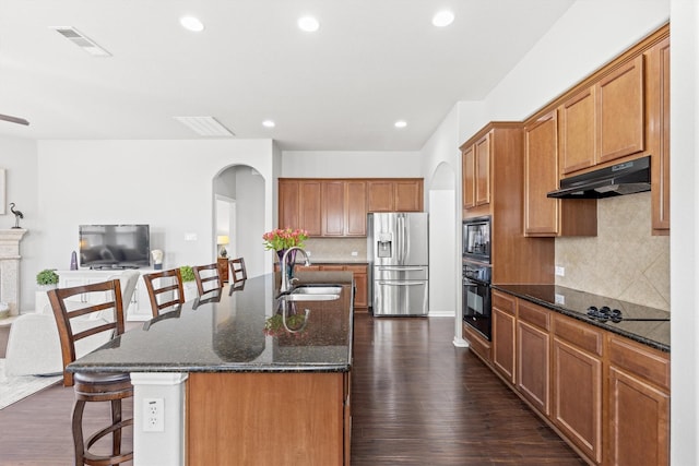 kitchen featuring a breakfast bar area, visible vents, a sink, under cabinet range hood, and black appliances