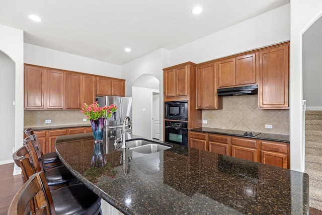 kitchen with black appliances, brown cabinetry, a sink, and under cabinet range hood