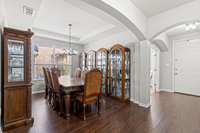 dining area with a notable chandelier, a raised ceiling, visible vents, dark wood-type flooring, and baseboards