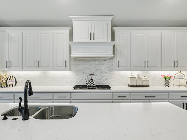 kitchen with light stone counters, stainless steel gas cooktop, a sink, white cabinets, and decorative backsplash