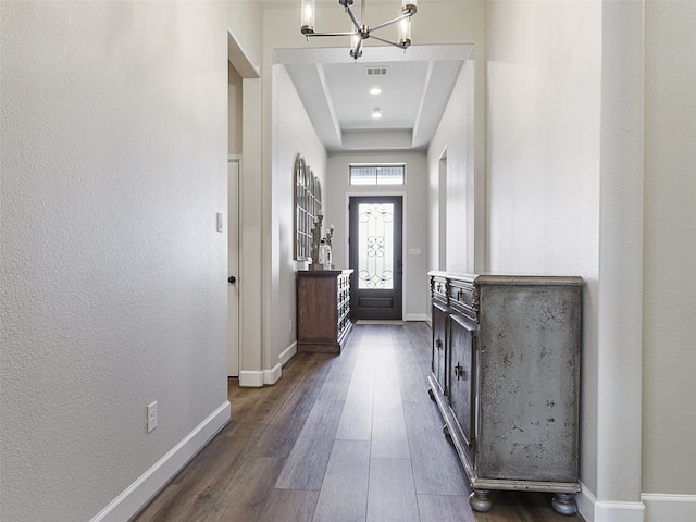 doorway with dark wood-style floors, a tray ceiling, visible vents, an inviting chandelier, and baseboards