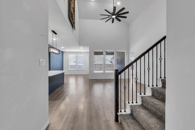 entrance foyer with stairway, a towering ceiling, a ceiling fan, wood finished floors, and baseboards