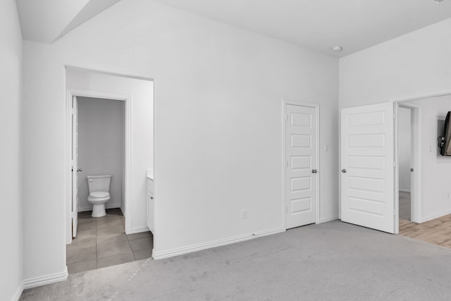 unfurnished bedroom with light carpet, ensuite bath, baseboards, and lofted ceiling