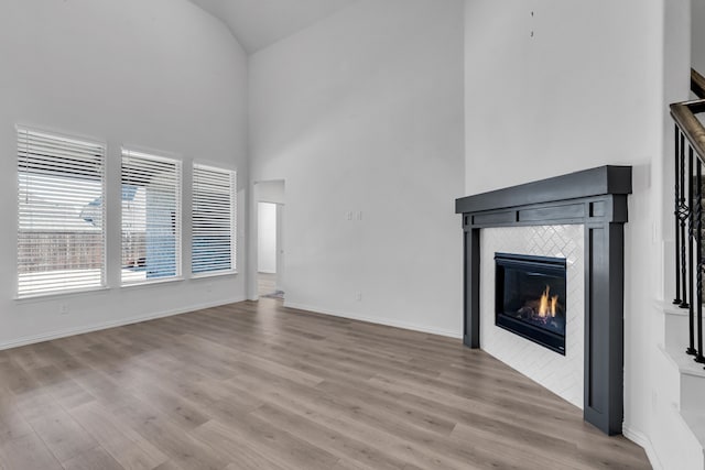 unfurnished living room featuring high vaulted ceiling, wood finished floors, a tile fireplace, and baseboards