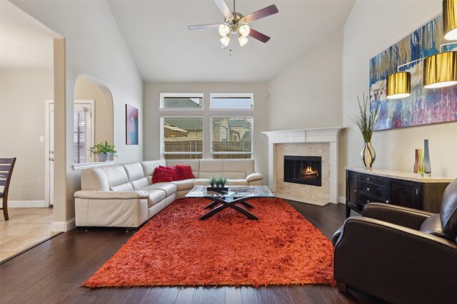 living room with high vaulted ceiling, a tile fireplace, ceiling fan with notable chandelier, baseboards, and hardwood / wood-style floors