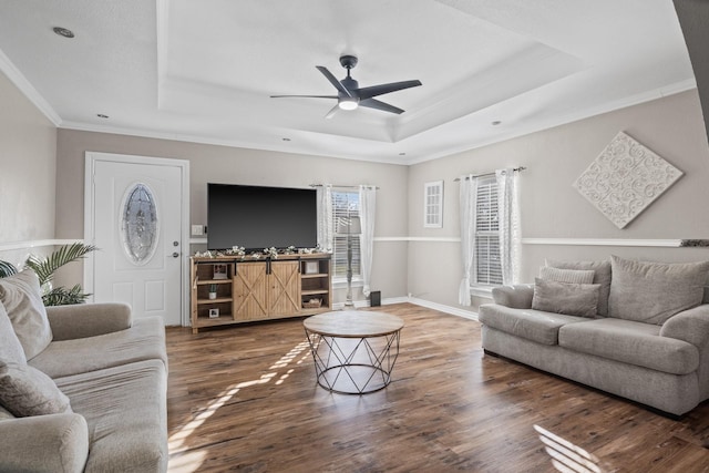 living room with ceiling fan, a tray ceiling, wood finished floors, and ornamental molding