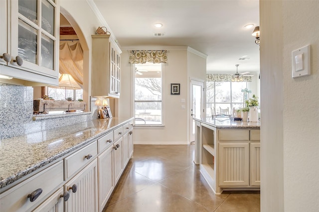 kitchen featuring light stone counters, light tile patterned flooring, glass insert cabinets, and baseboards