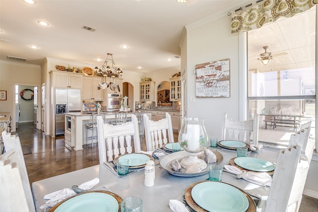 dining room featuring arched walkways, ornamental molding, ceiling fan with notable chandelier, and visible vents