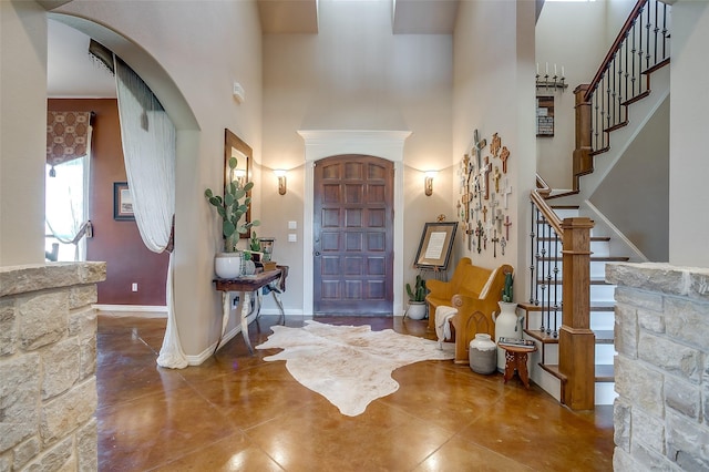 foyer entrance with arched walkways, stairway, a towering ceiling, finished concrete floors, and baseboards