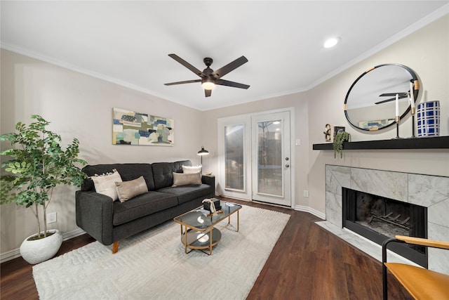 living room with crown molding, a ceiling fan, a high end fireplace, wood finished floors, and baseboards