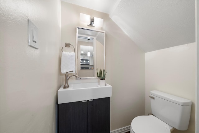 bathroom with vaulted ceiling, a textured ceiling, vanity, and toilet