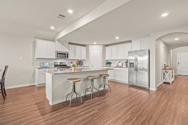 4137 Agatha Ln, Celina, TX 76227 - kitchen featuring stainless steel appliances, arched walkways, light wood-type flooring, decorative backsplash, and an island with sink
