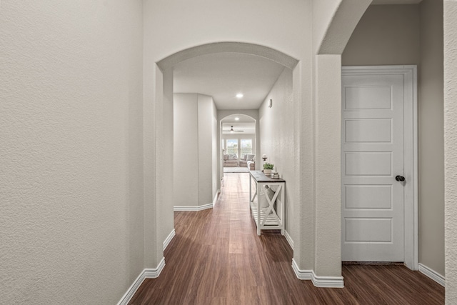 corridor with dark wood-type flooring, arched walkways, a textured wall, and baseboards