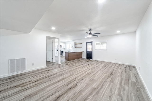 unfurnished living room featuring light wood finished floors, visible vents, ceiling fan, a sink, and baseboards