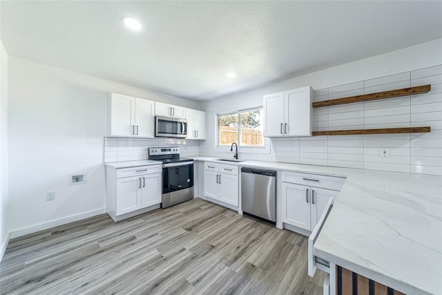 kitchen with a sink, appliances with stainless steel finishes, light wood-type flooring, decorative backsplash, and open shelves