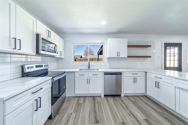 kitchen featuring stainless steel appliances, open shelves, a sink, a textured ceiling, and backsplash