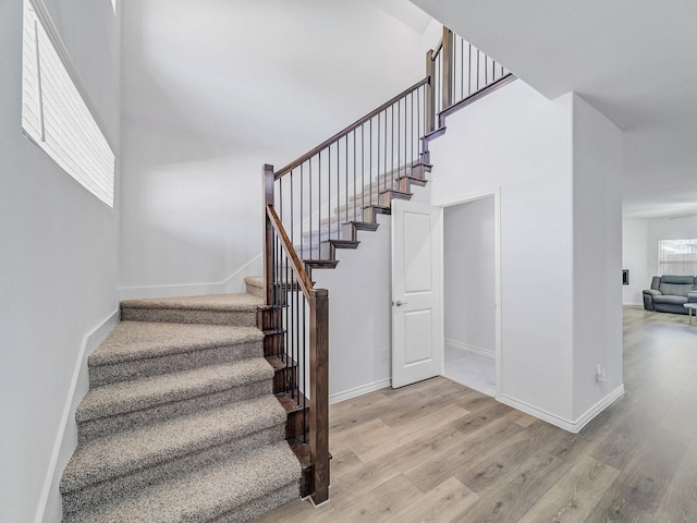 staircase featuring a towering ceiling, baseboards, and wood finished floors